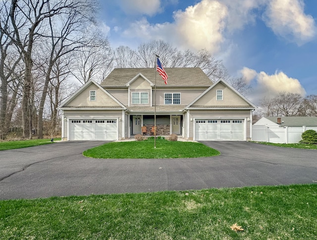 craftsman-style home with a front lawn, covered porch, fence, a garage, and aphalt driveway
