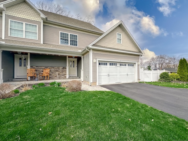 traditional-style house featuring driveway, fence, a front yard, and covered porch