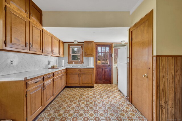 kitchen with light countertops, freestanding refrigerator, brown cabinets, backsplash, and light floors