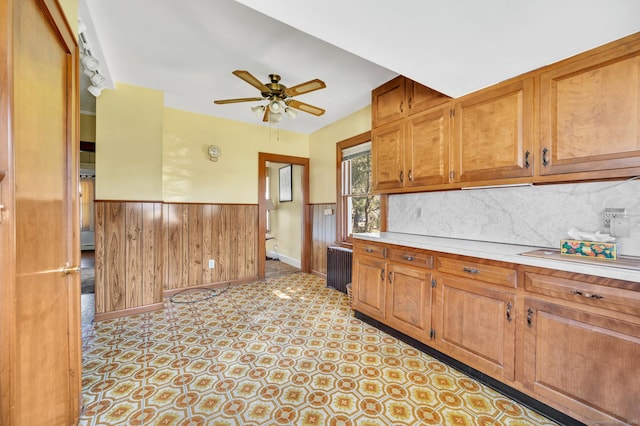 kitchen featuring brown cabinets, light countertops, a wainscoted wall, and wooden walls