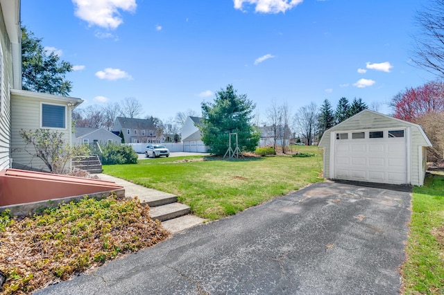 view of yard with an outbuilding, aphalt driveway, a detached garage, and fence