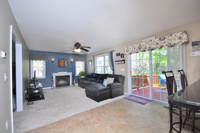 carpeted living area with a glass covered fireplace, baseboards, ceiling fan, and a textured ceiling