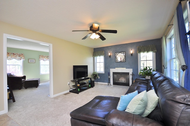 carpeted living room featuring baseboards, a glass covered fireplace, and ceiling fan