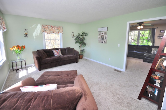 carpeted living area featuring baseboards, a ceiling fan, a textured ceiling, and a healthy amount of sunlight