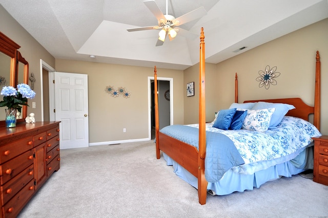 bedroom featuring visible vents, baseboards, ceiling fan, light colored carpet, and a tray ceiling