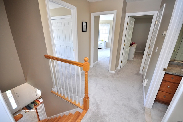 hall with light colored carpet, baseboards, and an upstairs landing