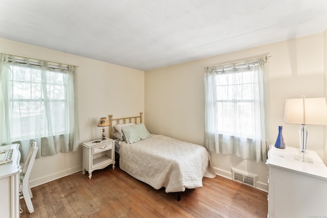 bedroom featuring hardwood / wood-style floors, baseboards, multiple windows, and visible vents
