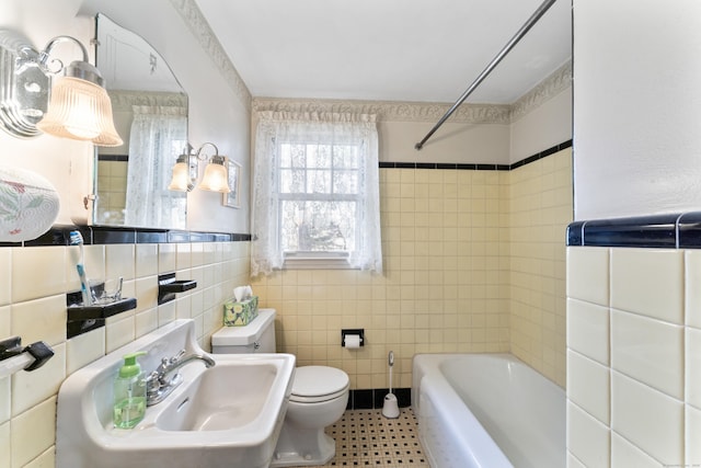 full bath with bathing tub / shower combination, a wainscoted wall, toilet, a sink, and tile walls