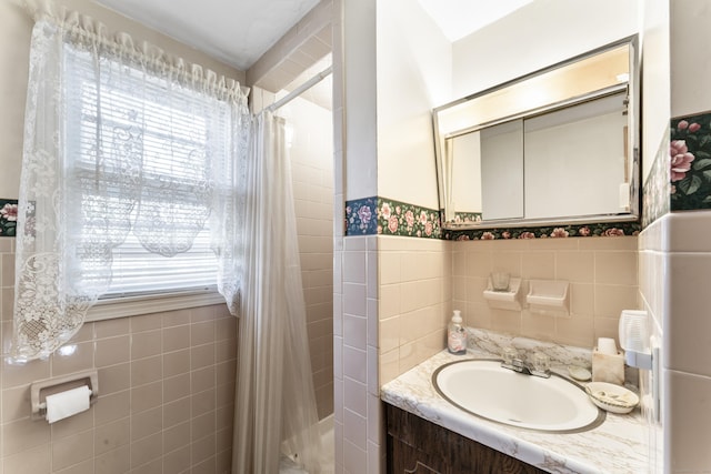 full bathroom with vanity, tile walls, a tile shower, and a wainscoted wall
