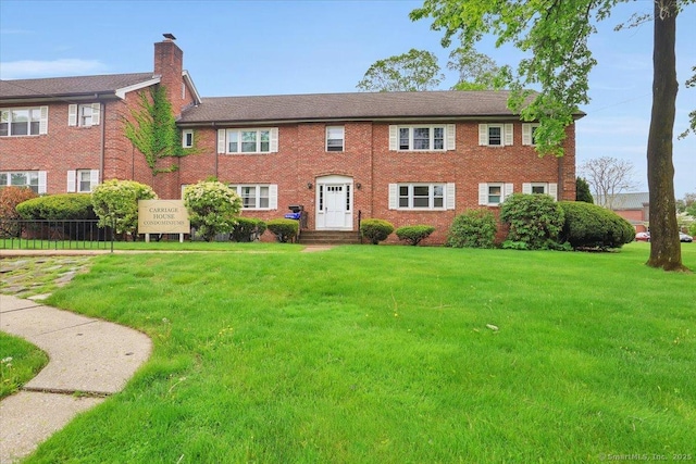 view of front facade with a chimney, a front lawn, and brick siding