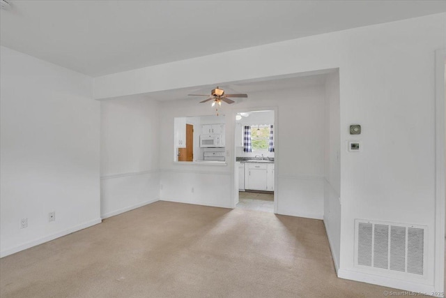 spare room featuring a ceiling fan, light colored carpet, and baseboards