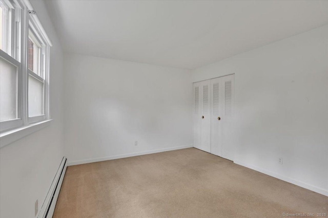 empty room featuring a baseboard radiator, light colored carpet, and baseboards
