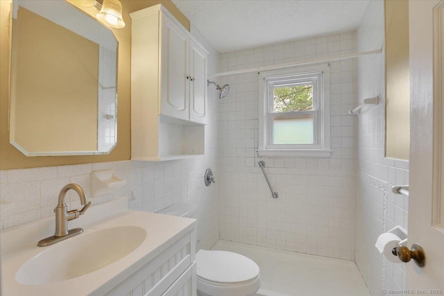 full bathroom featuring tile walls, tiled shower, toilet, and vanity