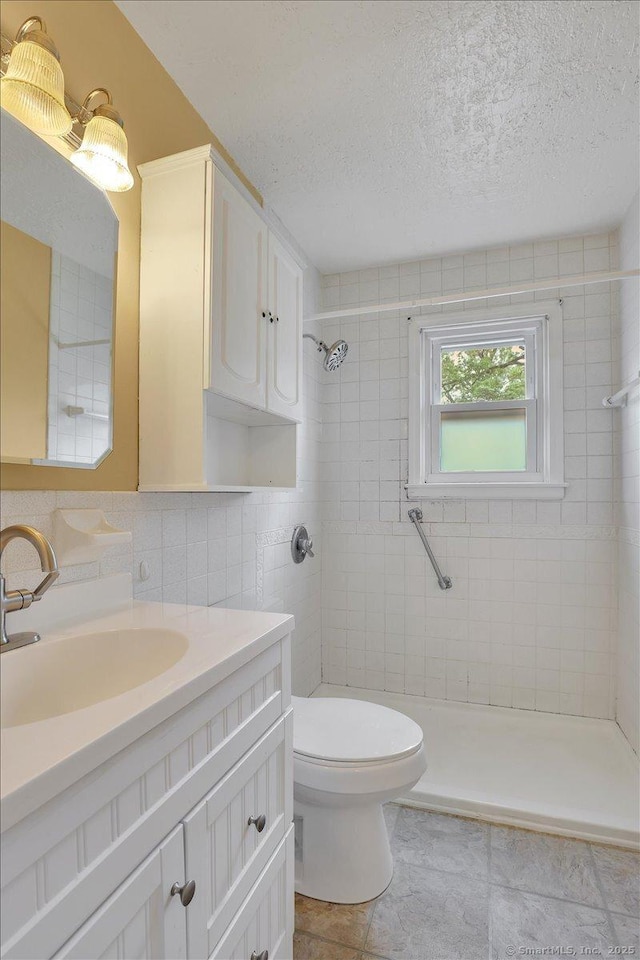 full bathroom featuring a stall shower, toilet, a textured ceiling, vanity, and tile walls