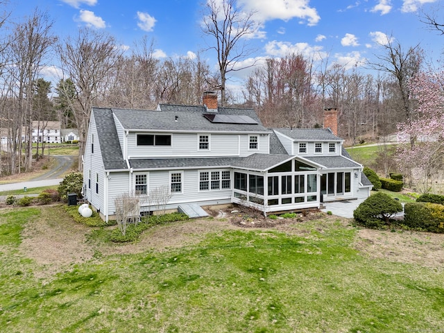 rear view of property with a chimney, a yard, solar panels, and a sunroom