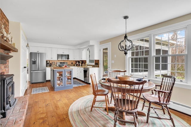 dining room featuring a wood stove, an inviting chandelier, a baseboard radiator, and light wood-type flooring