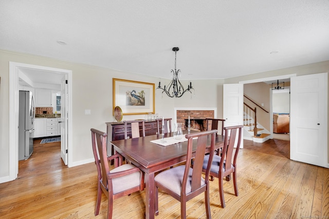 dining area with light wood-style flooring, a chandelier, baseboards, a fireplace, and stairs
