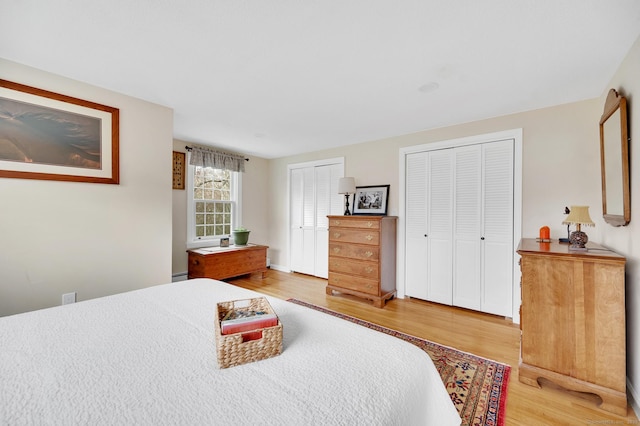 bedroom with multiple closets, wood finished floors, and a baseboard radiator