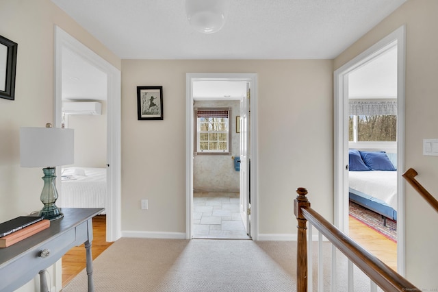 hallway featuring baseboards, a wall mounted air conditioner, and an upstairs landing