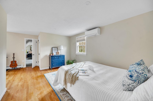 bedroom with a baseboard heating unit, light wood finished floors, a wall mounted air conditioner, and baseboards