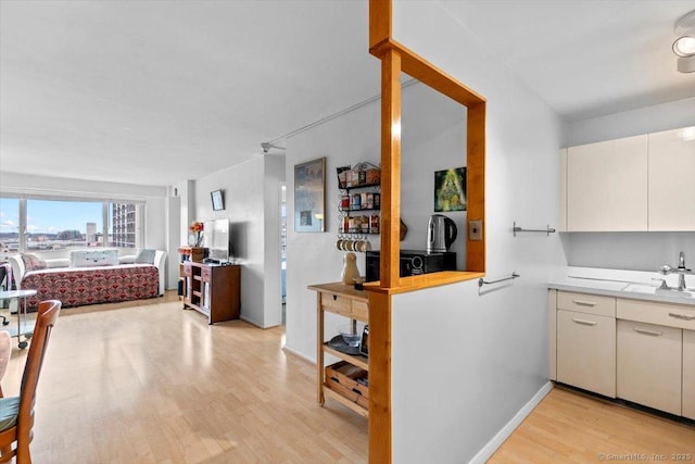 kitchen with light wood-style flooring, white cabinets, a sink, light countertops, and open floor plan