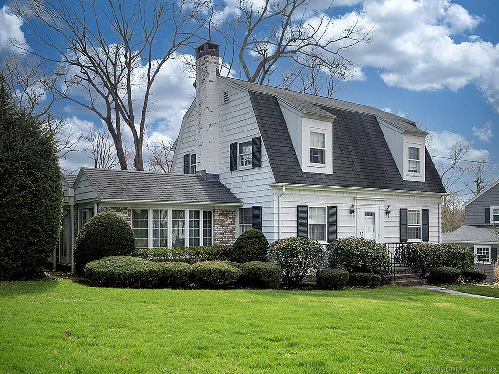 colonial inspired home featuring a front yard, a shingled roof, a gambrel roof, and a chimney