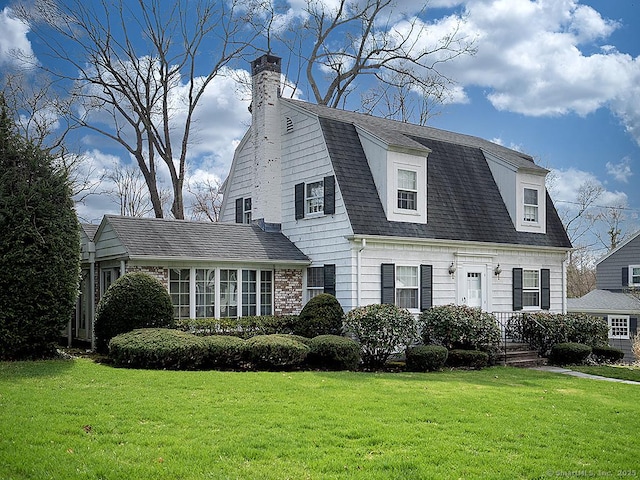 colonial inspired home featuring a front yard, a shingled roof, a gambrel roof, and a chimney