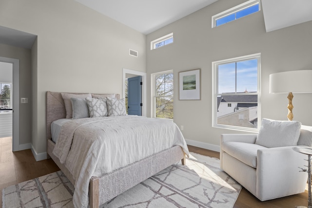 bedroom with baseboards, wood finished floors, visible vents, and a high ceiling