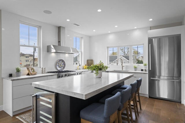 kitchen with wall chimney exhaust hood, wine cooler, freestanding refrigerator, visible vents, and modern cabinets