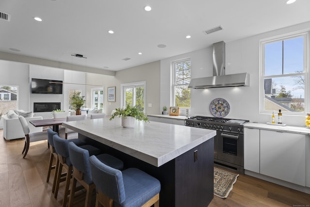 kitchen with visible vents, a kitchen island, wall chimney exhaust hood, double oven range, and dark wood-style flooring