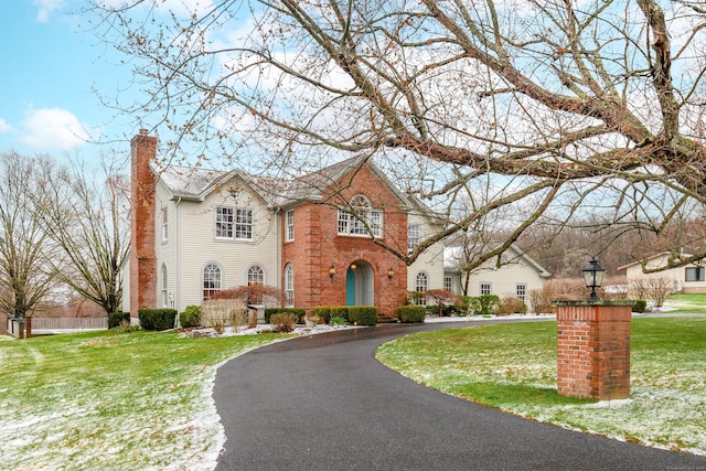 view of front of property featuring brick siding, curved driveway, a chimney, and a front lawn