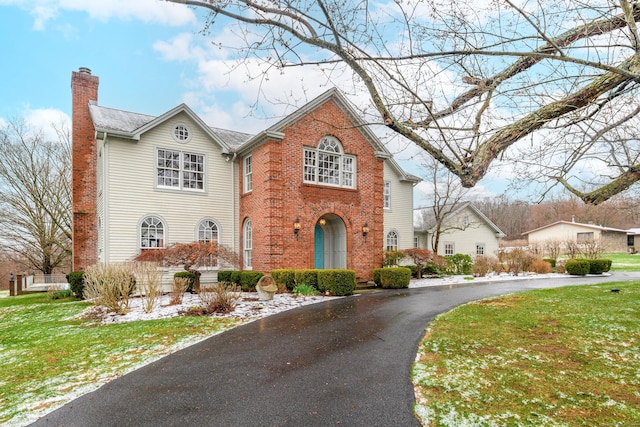 traditional home with brick siding, aphalt driveway, a chimney, and a front lawn
