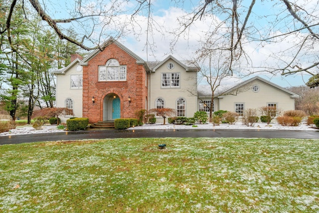 traditional home featuring brick siding, a chimney, and a front yard