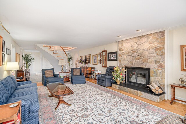 living room featuring stairway, crown molding, and a stone fireplace