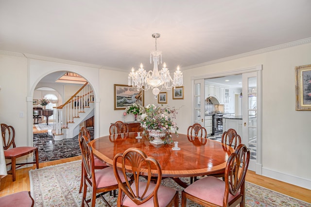 dining room with crown molding, light wood-style floors, stairway, arched walkways, and a notable chandelier