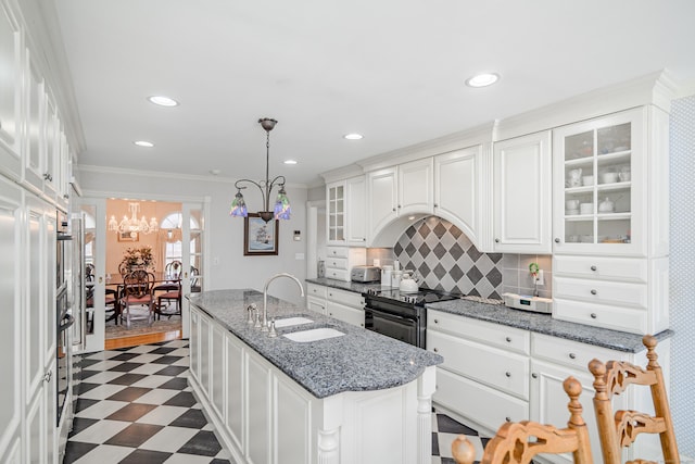kitchen featuring a sink, a kitchen island with sink, dark floors, a chandelier, and white cabinetry