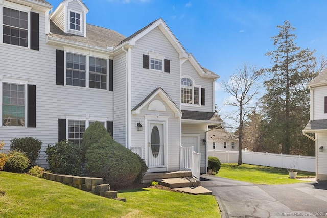 view of front of house featuring fence, a shingled roof, and a front lawn