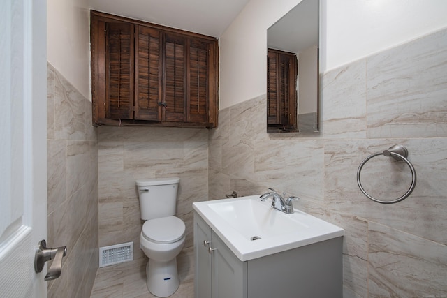 bathroom featuring vanity, a wainscoted wall, toilet, visible vents, and tile walls