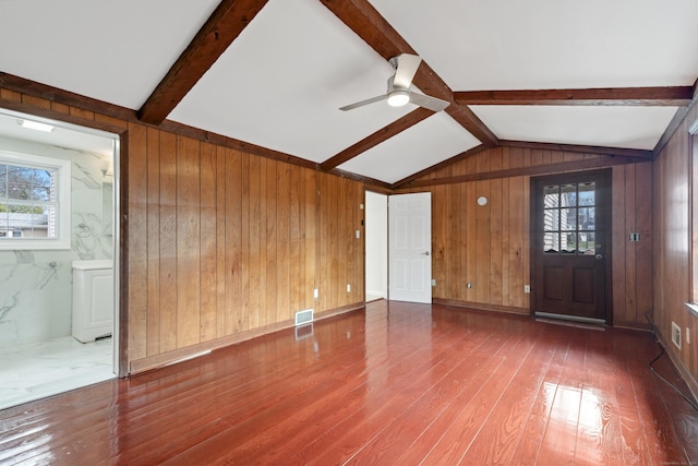 unfurnished living room featuring wooden walls, a ceiling fan, wood finished floors, and lofted ceiling with beams