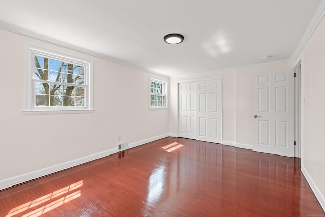 unfurnished bedroom with a closet, baseboards, ornamental molding, visible vents, and wood finished floors