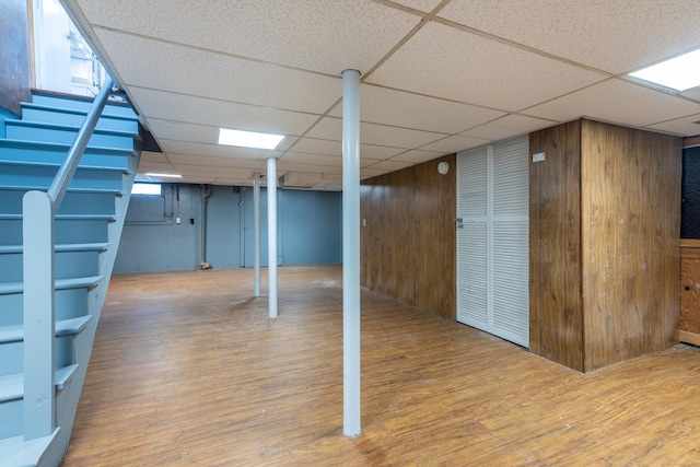 basement featuring stairway, a drop ceiling, wooden walls, and wood finished floors