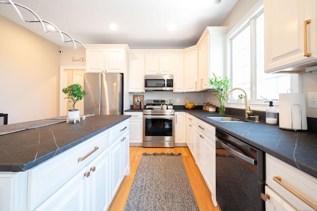 kitchen with white cabinets, light wood-style flooring, a sink, dark countertops, and appliances with stainless steel finishes