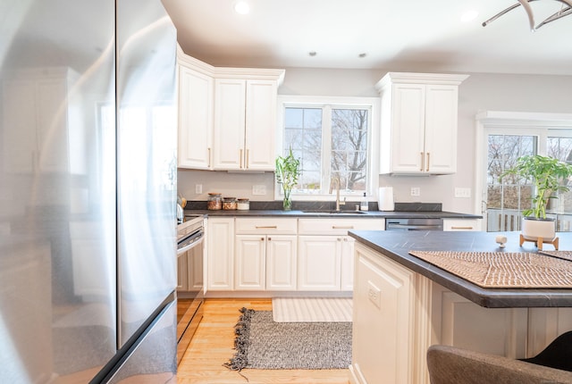 kitchen featuring dark countertops, a sink, light wood-style flooring, appliances with stainless steel finishes, and a breakfast bar area