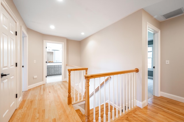 hallway with light wood finished floors, baseboards, visible vents, and an upstairs landing