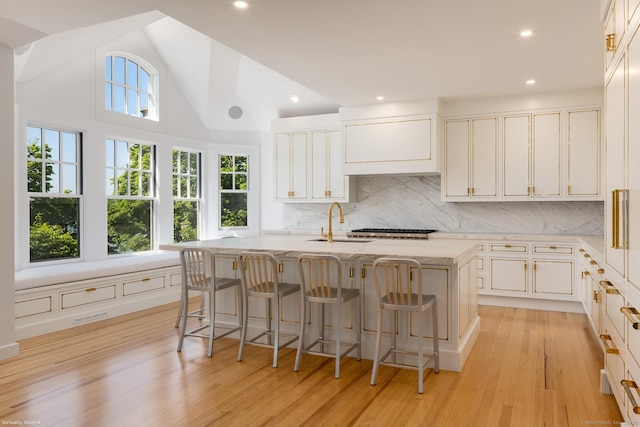 Rogers Is, Branford, CT 06405 - kitchen with a kitchen island with sink, light wood-type flooring, tasteful backsplash, white cabinets, and lofted ceiling