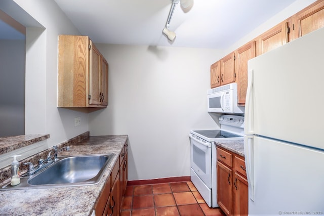 kitchen with track lighting, baseboards, a sink, dark tile patterned floors, and white appliances