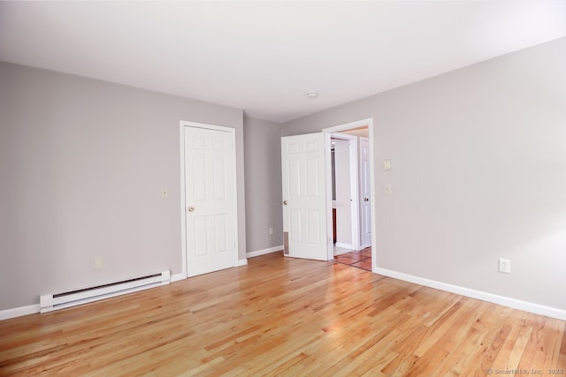 empty room featuring light wood-style floors, a baseboard heating unit, and baseboards