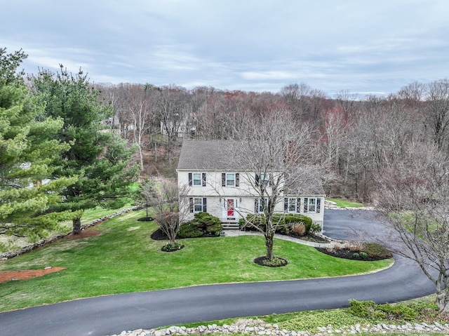 view of front of home with a front yard, a view of trees, and aphalt driveway