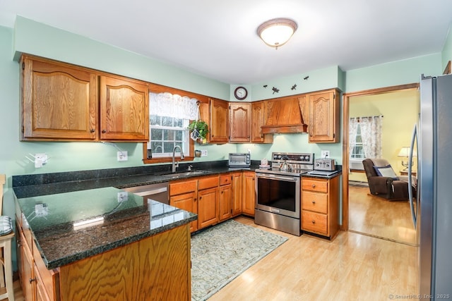 kitchen with light wood-style floors, brown cabinetry, appliances with stainless steel finishes, a sink, and custom range hood
