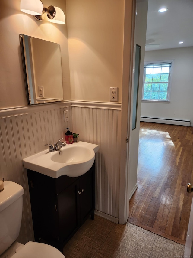 half bathroom with a baseboard radiator, toilet, a wainscoted wall, and vanity